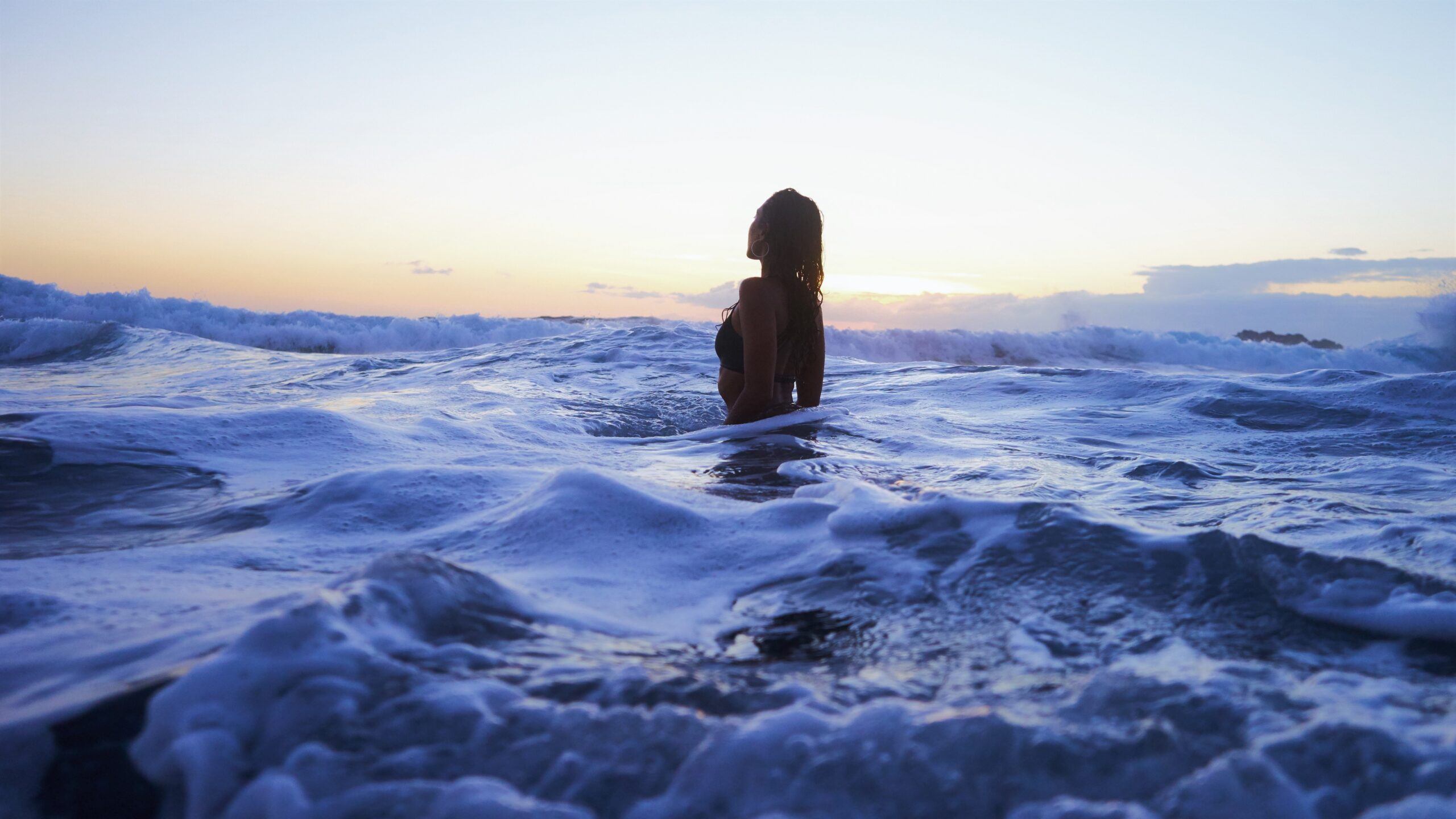 A woman treading water in the ocean at sunset