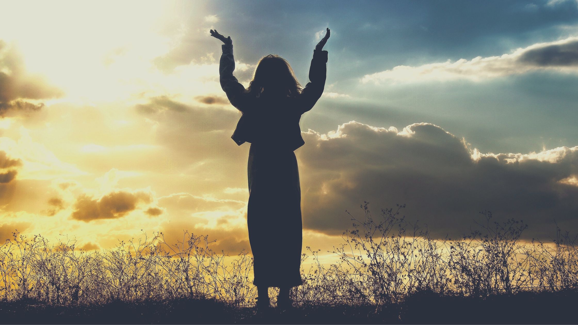 A woman raising her hands at dusk