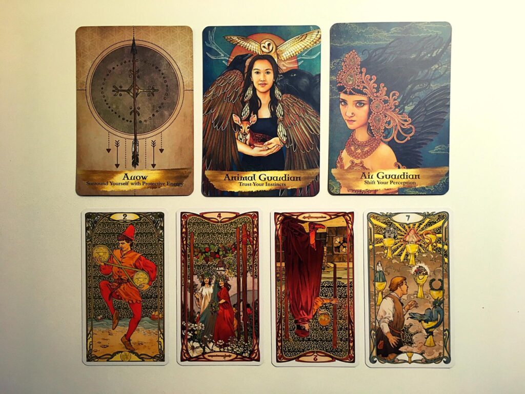 Arrow, Animal Guardian, and Air Guardian cards from the Angels and Ancestors Oracle deck; the Two of Pentacles, Four of Wands, Two of Wands Reversed, and Seven of Cups from the Golden Art Nouveau Tarot Deck