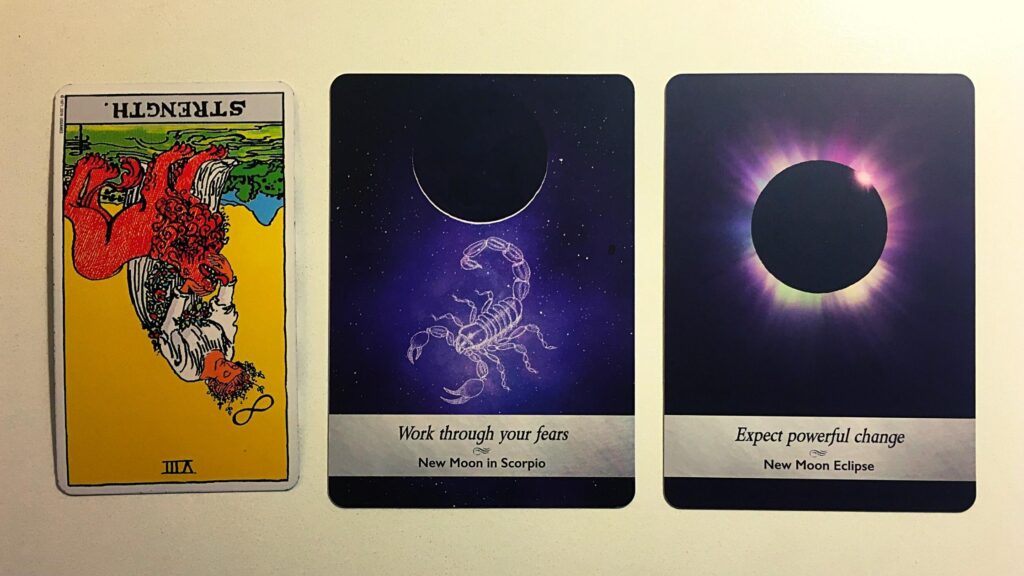 Strength, Reversed from the Rider-Waite tarot deck; the New Moon in Scorpio and New Moon Eclipse from the Moonology Oracle deck